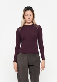 Fitted, langromige top in diep bordeaux ribbelstof met kantaccenten op de schouders en een gegolfde halslijn, gecombineerd met gestructureerde grijze broek.