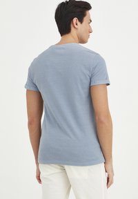 Svetlomodré tričko, krátke rukávy s prehnutými manžetami, úzky strih, vyrobené z mäkkej látky, zobrazené zozadu s okrúhlym výstrihom.