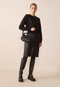 Czarny sweter z dzianiny, skórzana spódnica ołówkowa z rozcięciem z przodu, czarne kozaki za kolano i czarna torebka na ramię. Gładkie tekstury i elegancki design.