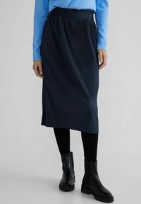 Dark navy pleated skirt with a wide waistband, paired with black ankle boots and black leggings. Soft texture, knee-length design.