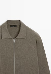 Grauer Strick-Pullover mit Reißverschluss, mit flachem Kragen und silbernem Reißverschluss. Die Textur ist glatt mit einem feinen, gleichmäßigen Muster. Etikett am Halsausschnitt sichtbar.