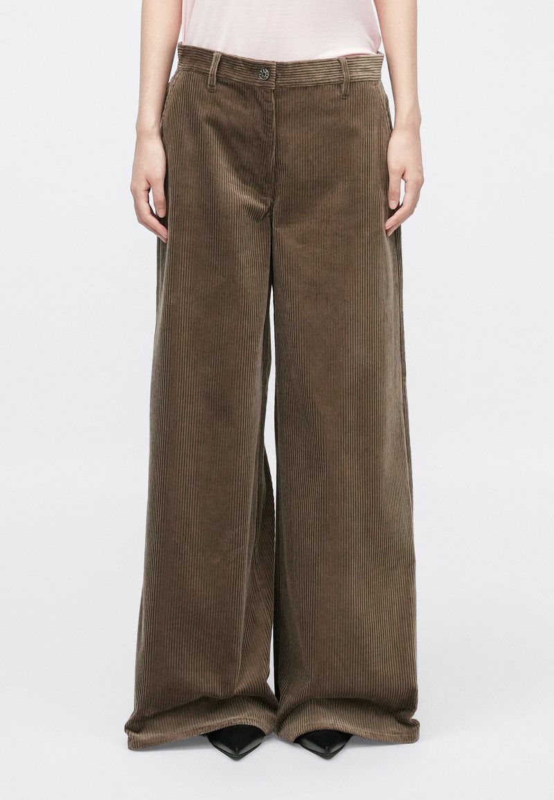 Wide-leg corduroy pants in dark brown, featuring vertical ribbed texture, front button closure, and side pockets, paired with black heels.