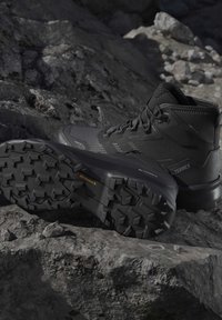 Black high-top hiking boots with textured Continental rubber soles placed on rocky terrain.