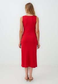 Rode mouwloze midi-jurk met een getailleerd silhouet, gladde textuur en een ronde halslijn, gecombineerd met lichtgekleurde hakken sandaaltjes.