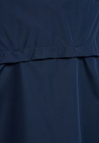 Primo piano di tessuto blu navy con cucitura orizzontale e dettaglio di cuciture arricciate.