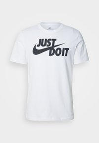 Vit bomullströja med en framträdande svart "JUST DO IT"-logotyp med en swoosh-design, rund hals och korta ärmar.