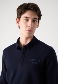 Námořnická modrá polokošile vyrobená z měkké látky, s límcem, knoflíkovou légou a jemným logem Porsche BOSS na hrudi.