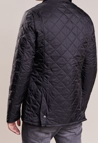 Veste matelassée noire avec un motif en losange, dotée d'un col montant et d'une fermeture par bouton-pression en bas, fabriquée à partir d'un matériau extérieur lisse.