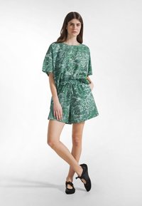 Groen kort mouw outfit met een bladpatroon, voorzien van een elastische tailleband en zijzakken. Gecombineerd met zwarte schoenen.