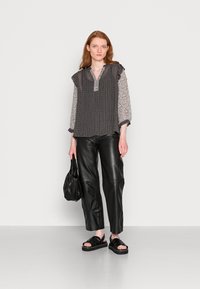 Blusa com padrão preto e branco, com ombros franzidos, combinada com calças de couro pretas de cintura alta e sandálias pretas com tiras.