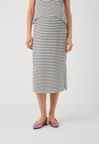 Černobílá pruhovaná midi sukně s bočním rozparkem, vyrobená z měkké tkaniny. V kombinaci s lesklými růžovými balerínami.