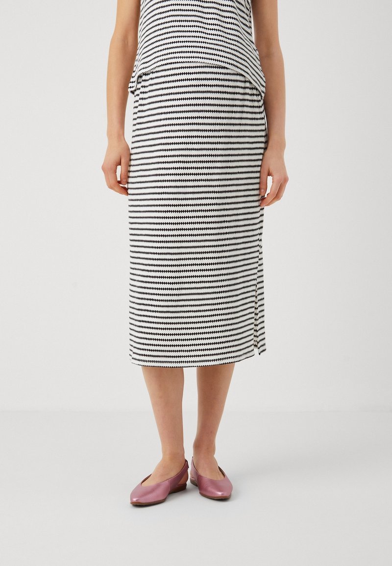 Černobílá pruhovaná midi sukně s bočním rozparkem, vyrobená z měkké tkaniny. V kombinaci s lesklými růžovými balerínami.