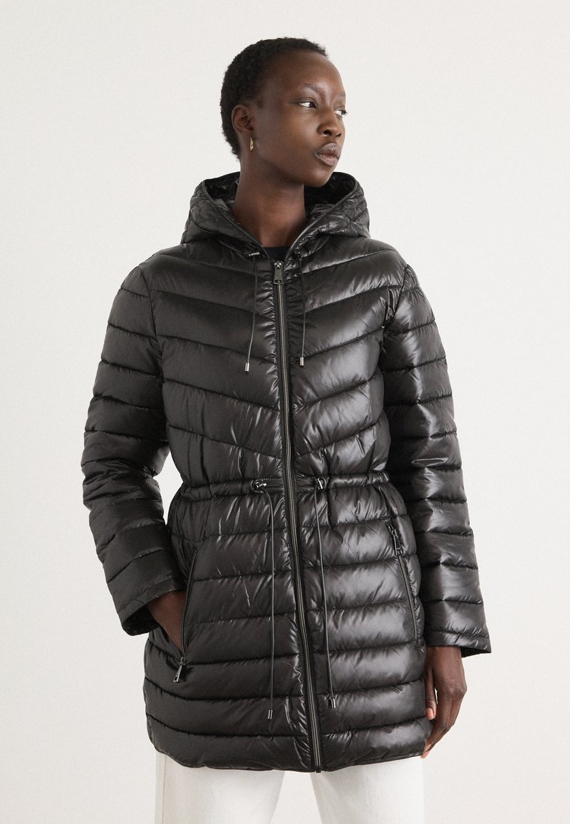 Doudoune noire avec capuche, présentant un design matelassé, une taille avec cordon de serrage, des poches latérales et une texture brillante.