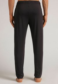 Schwarze, leichte Hose mit elastischem Bund und geradem Bein im Blick von hinten, barfuß.