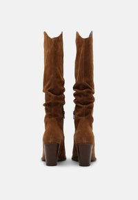 Brązowe kozaki za kolano zamszowe o luźnym kroju, zaokrąglonych noskach i obcasie typu bloczek. Posiadają zamki po zewnętrznej stronie ułatwiające zakładanie.