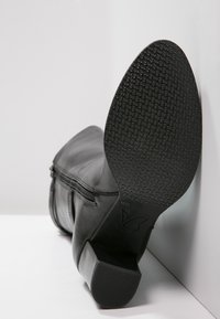 Black leather ankle boot with a low heel, textured rubber sole, and zip closure detail on the side, positioned at an angle.