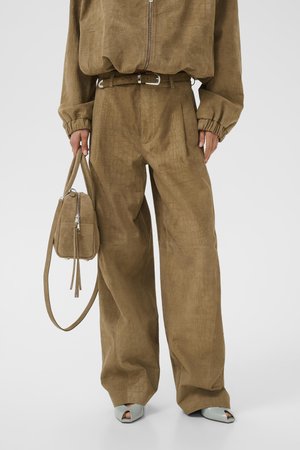 Hnedé široké nohavice s textúrou s pásom v rovnakom štýle, v kombinácii so zapínaným topom, svetlosivými sandálmi s otvorenou špičkou a malou kabelkou v rovnakom štýle.