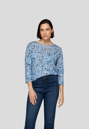 Haut à motif bleu avec des manches trois-quarts, mettant en avant un imprimé circulaire dans différentes nuances de bleu. Assorti à un jean en denim foncé.
