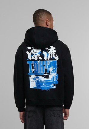 Svart hettegenser med et grafisk trykk på ryggen med blå detaljer, som viser en animekarakter og en bil, i en livlig, tegneseriestil.