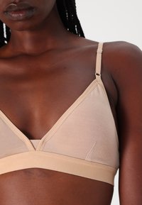 Soutien-gorge sans fil beige clair avec un design en V, des bretelles ajustables et une texture douce et lisse. La bande offre un ajustement confortable.