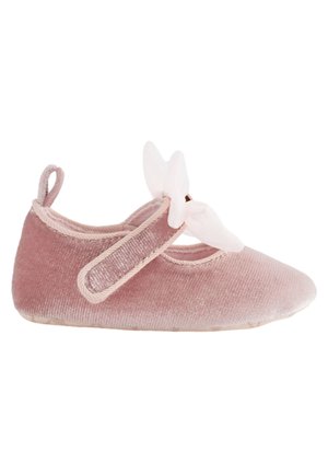 Zapato para bebé de terciopelo rosa suave con una cinta de velcro y un lazo decorativo blanco en la parte superior, exhibido sobre un fondo blanco.