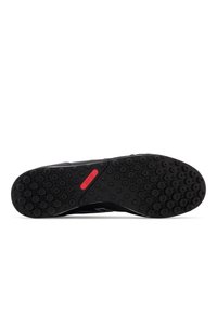 Black athletic shoe with a textured rubber outsole, featuring circular patterns and a small red accent near the heel. Minimalistic design.