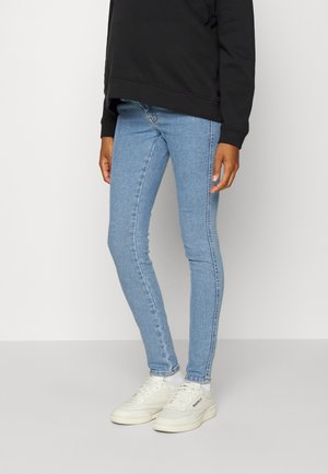 Jeans skinny em denim azul claro com uma textura suave, apresentando uma cintura de altura média e um design justo, combinados com ténis brancos.