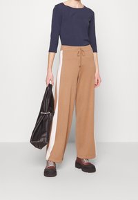Pantaloni larghi marroni con strisce bianche laterali, abbinati a una maglietta a maniche lunghe blu navy, borsa nera e stivaletti con suola spessa marroni.
