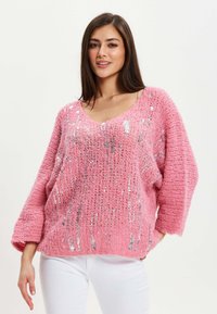 Pink knit sweater with a V-neck, wide sleeves, and silver sequins. Textured material with an oversized fit, showcasing a loose silhouette.