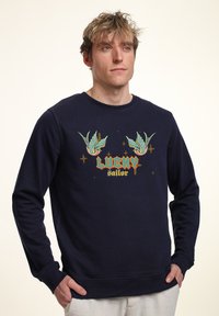 Felpa navy in cotone con maniche lunghe. Presenta una grafica colorata con due uccelli e la scritta "LUCKY sailor" in stile retrò.