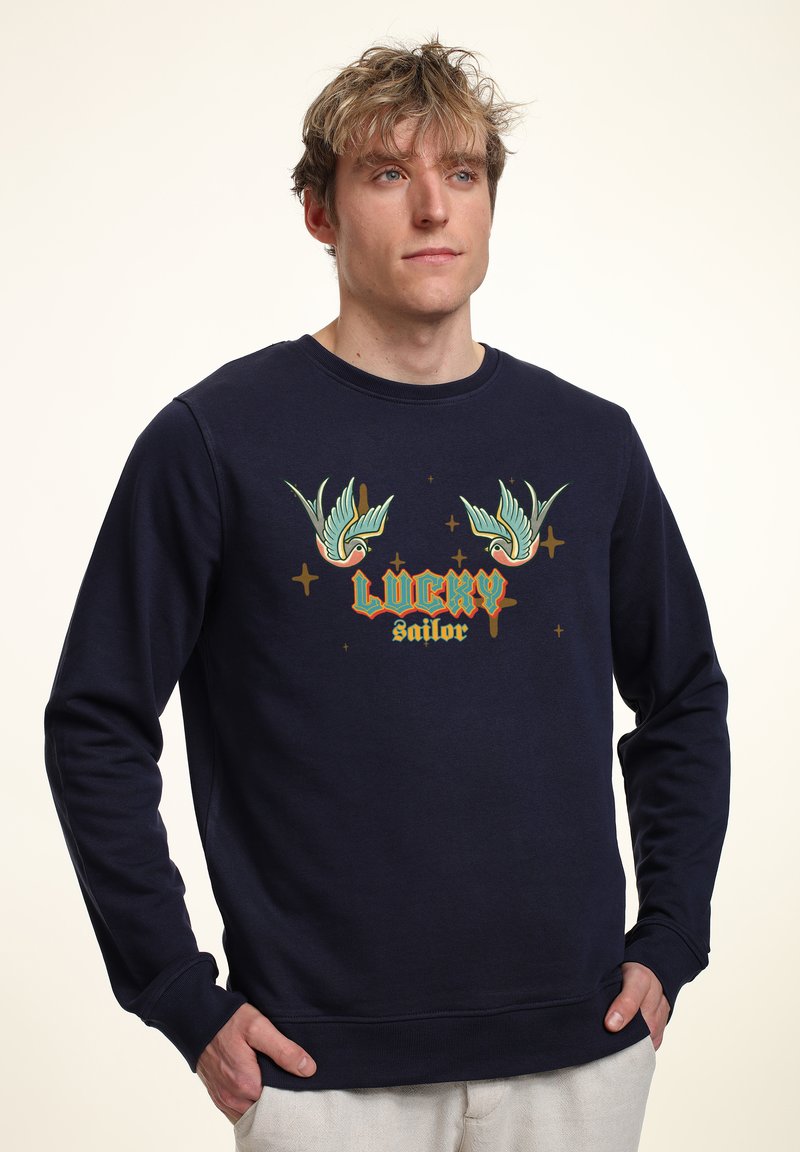 Felpa navy in cotone con maniche lunghe. Presenta una grafica colorata con due uccelli e la scritta "LUCKY sailor" in stile retrò.