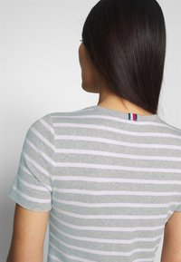 Camiseta de manga corta a rayas grises y blancas con textura acanalada. Presenta un pequeño detalle de etiqueta de color en la parte posterior del escote.