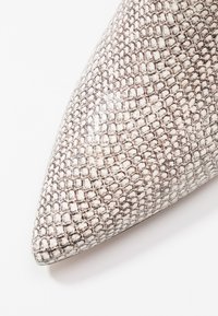 Pointed-toe shoe made of textured, faux snake leather in white and gray. Features a smooth surface with a raised, scaled pattern.