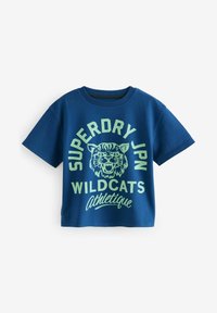 Camiseta de algodón azul con cuello redondo; presenta un estampado gráfico verde de un felino salvaje y el texto: "SUPERDRY JPN WILDCATS Athletique." Mangas cortas.