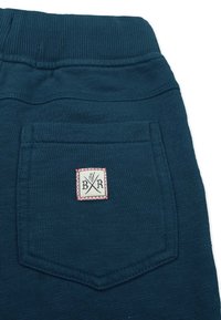 Teal bomullsbyxor har en ribbad midja, en patchficka med en dekorativ etikett och en texturerad, mjuk tyg.