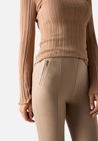 Top de manga larga con canalé en suave beige, combinado con leggings ajustados beige que cuentan con un bolsillo lateral con cremallera y una textura suave.