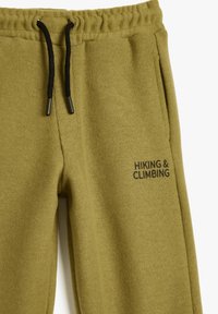 Olijfgroene sweatpants in een geribde textuur, met een zwarte trekkoord en de tekst "Wandelen & Klimmen" aan de zijkant.