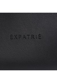 Surface en cuir noir texturé avec le mot « EXPATRIÉ » embossé en lettres majuscules au centre.