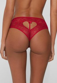 Rote Spitzen-String mit herzförmigem Ausschnitt auf der Rückseite, verziert mit einer kleinen Schleife, mit weicher Textur und niedrigem Bund.