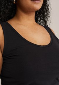 Svart tanktop i slät tyg, med en scallopad halsringning och åtsittande passform, som visar en ren och minimalistisk stil.