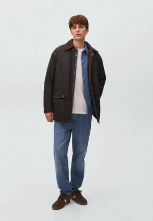 Brown cotton jacket with a brown collar, layered over a blue shirt and white t-shirt, paired with light blue jeans and brown sneakers.