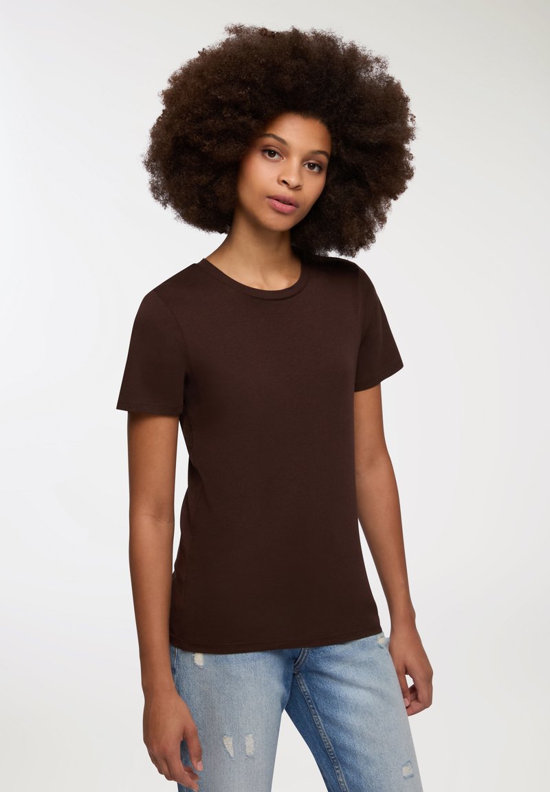 Brązowa bluzka z krótkim rękawem z miękkiego materiału z klasycznym okrągłym dekoltem, w połączeniu z jasnoniebieskimi, przetartymi dżinsami. Prosty i nowoczesny design.