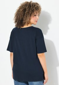 Camiseta de algodón azul marino con mangas cortas, cuello redondo y dobladillo recto. Incluye aberturas laterales y un diseño trasero limpio.