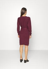 Burgundy stickad klänning med lång ärm, figursydd midja och lätt scallopad fåll. Bärs med svarta klackmules.