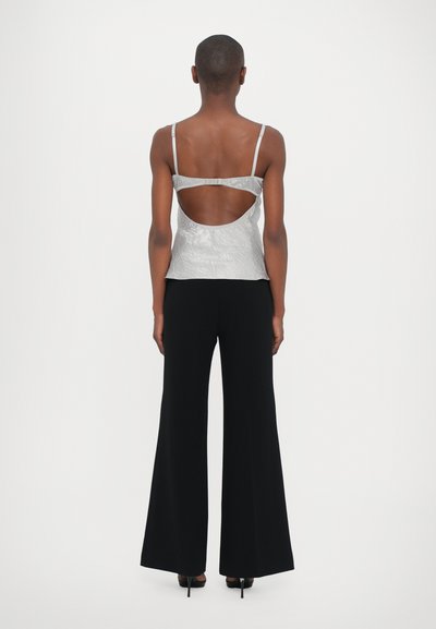 Top plateado sin mangas con un acabado texturizado y diseño de espalda abierta, combinado con pantalones de campana negros y tacones altos.