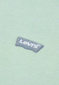 Υφασμα ανοιχτοπράσινο με υφή ύφανσης, με ένα γκρι κεντημένο έμβλημα του λογότυπου Levi's στην κάτω αριστερή γωνία.