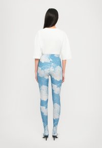 Leggings con un estampado de denim azul y gráficos de nubes blancas, combinados con una camiseta blanca básica de gran tamaño y zapatos de tacón negros.