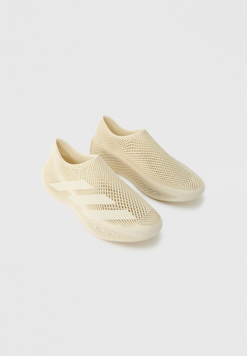Ζευγάρι μπεζ παπούτσια slip-on με πλέγμα, δίχτυ δομή και τρεις λεπτομέρειες με ρίγες σε απλό ανοιχτό γκρι φόντο.
