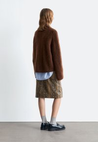 Brauner, flauschiger Pullover, hellblaues Hemd darunter, Schlange-Muster Rock in Braun- und Goldtönen, graue Socken, schwarze Slipper. Einfaches und modernes Design.