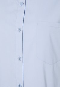 Chemise bleu clair avec quatre boutons visibles et une unique poche poitrine sur le côté droit.